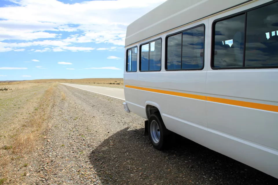 White microbus with yellow stripe on rural road with empty road and blue sky in background.